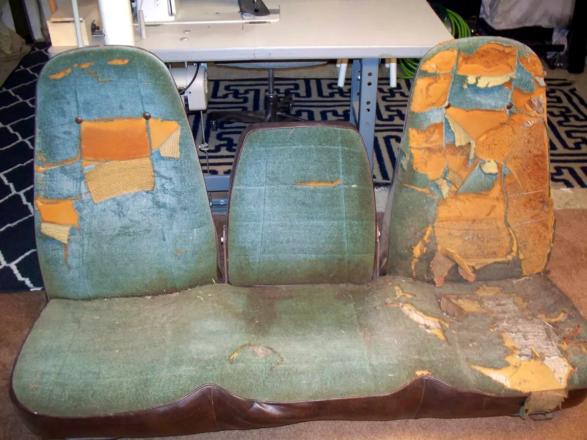 Worn vintage Road Runner-style bench seat with deteriorated fabric, damaged padding and aged upholstery before restoration
