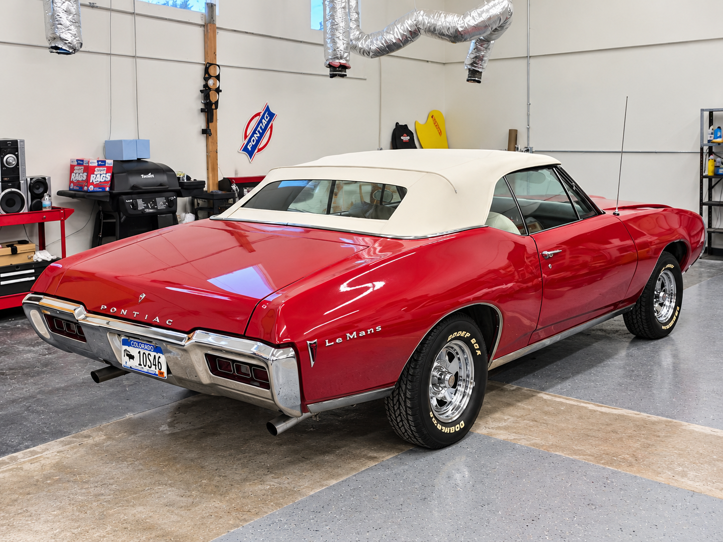 Glossy red classic Pontiac LeMans convertible with a white soft top inside an upholstery workshop