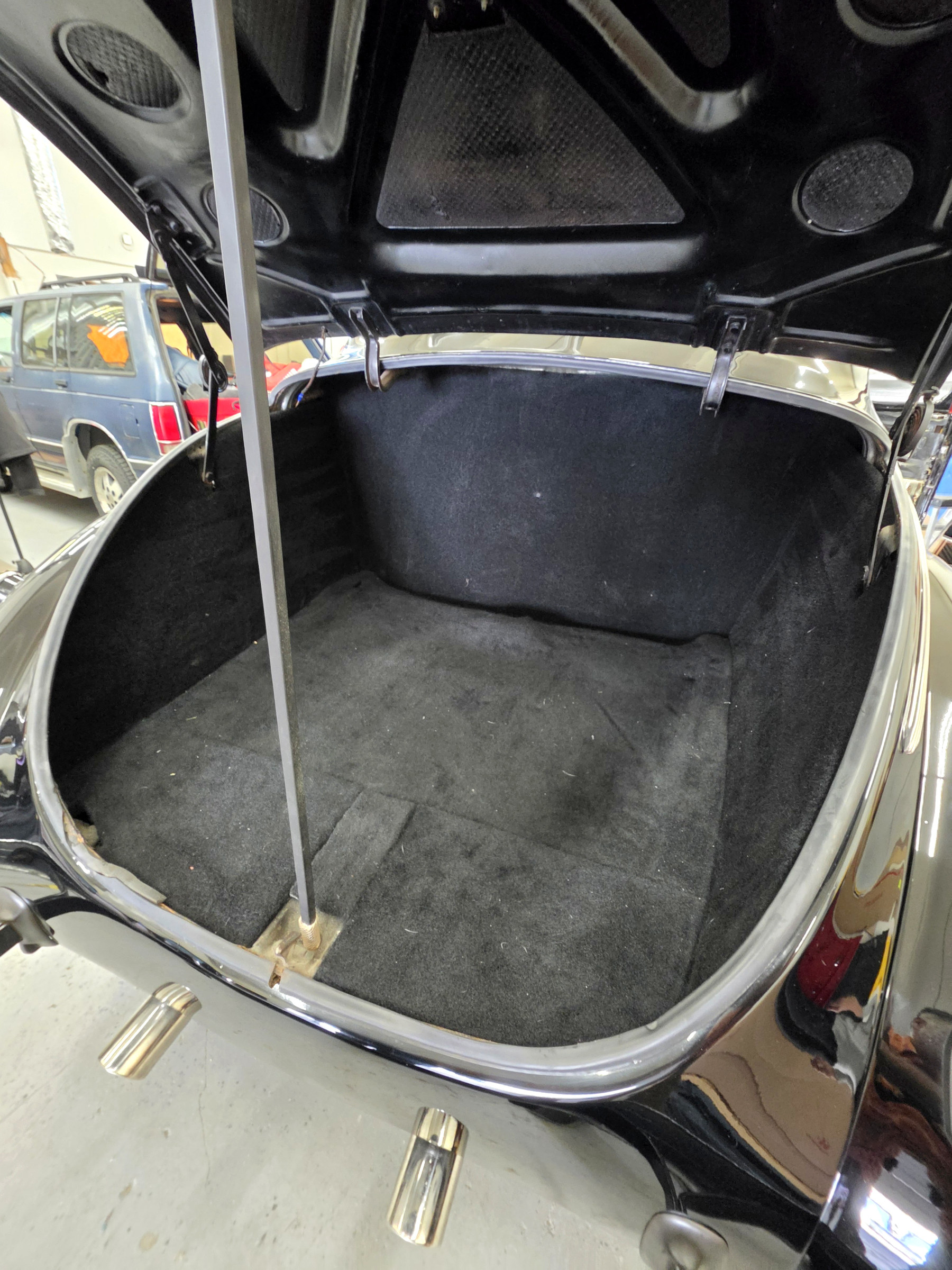 Restored classic car trunk with fitted dark carpeting and upholstered rear panel, first angle