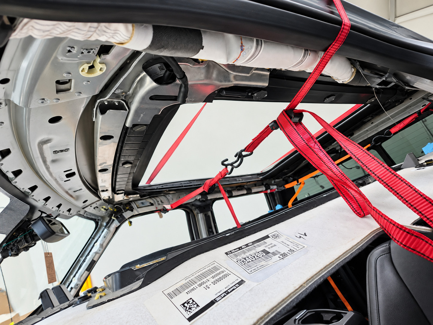 Headliner removed from SUV roof exposing the side curtain airbag zone, metal roof structure and red support straps