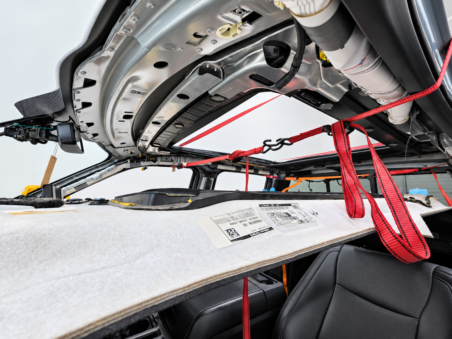 Vehicle sunroof frame exposed with lowered headliner board secured by red support straps during roof-trim work